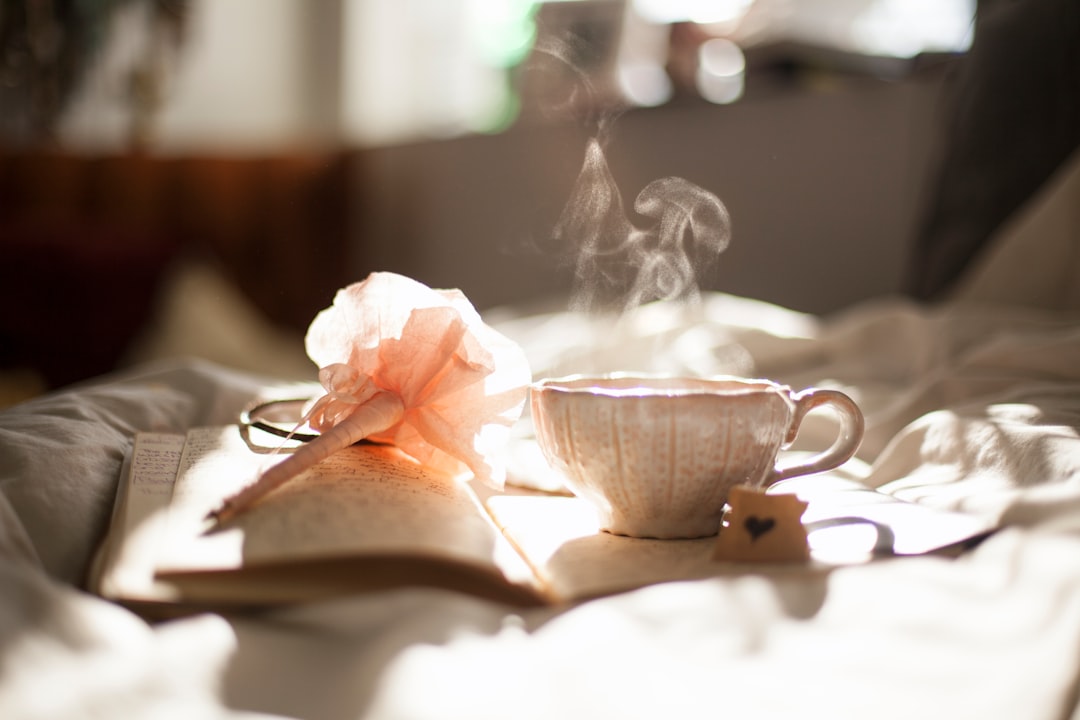 Person holding a morning coffee mug beside a small wellness softgel on a wooden countertop in calm morning light