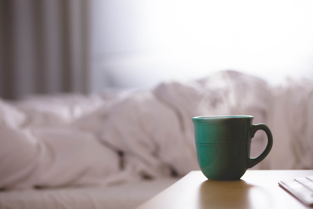 A calm morning kitchen scene with a glass of water, softgel capsules, and a cup of coffee on a wooden countertop.