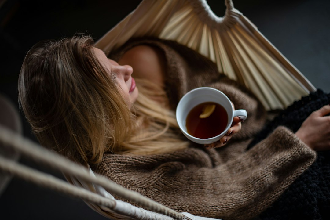 Person sitting quietly in a softly lit room at evening, hands around a warm mug, looking relaxed and present
