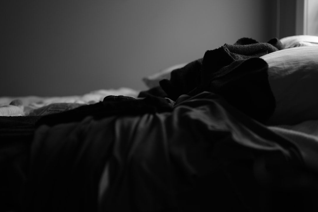 A glass of water and a small softgel on a nightstand beside a warm lamp in a quiet bedroom at night