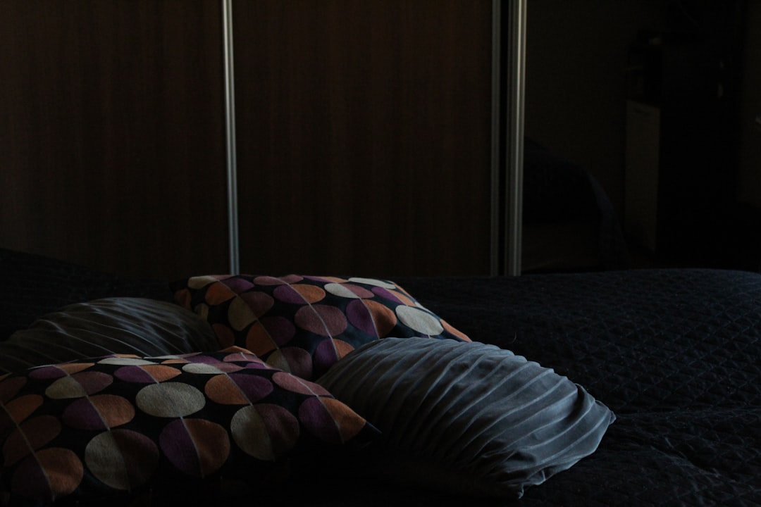 Person placing a softgel capsule on a nightstand beside a glass of water in a softly lit bedroom at night